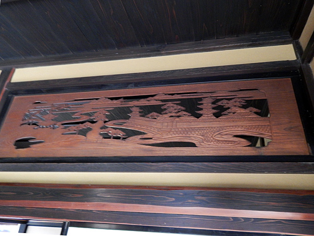 Резное деревянное панно над дверью. В центре — сцена из жизни японских богов